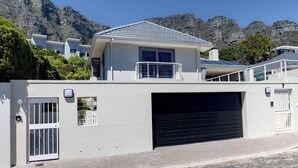 A modern house with a garage, a balcony, and a mountain backdrop. - Echo garden apartment in Camps Bay (Cape Town)