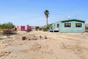 A desert landscape with a green mobile home, a pink building, and a palm tree. - 2BR/2BA Desert Winds SkyHouse –  desert hideaway with mountain views, (Desert Hot Springs)