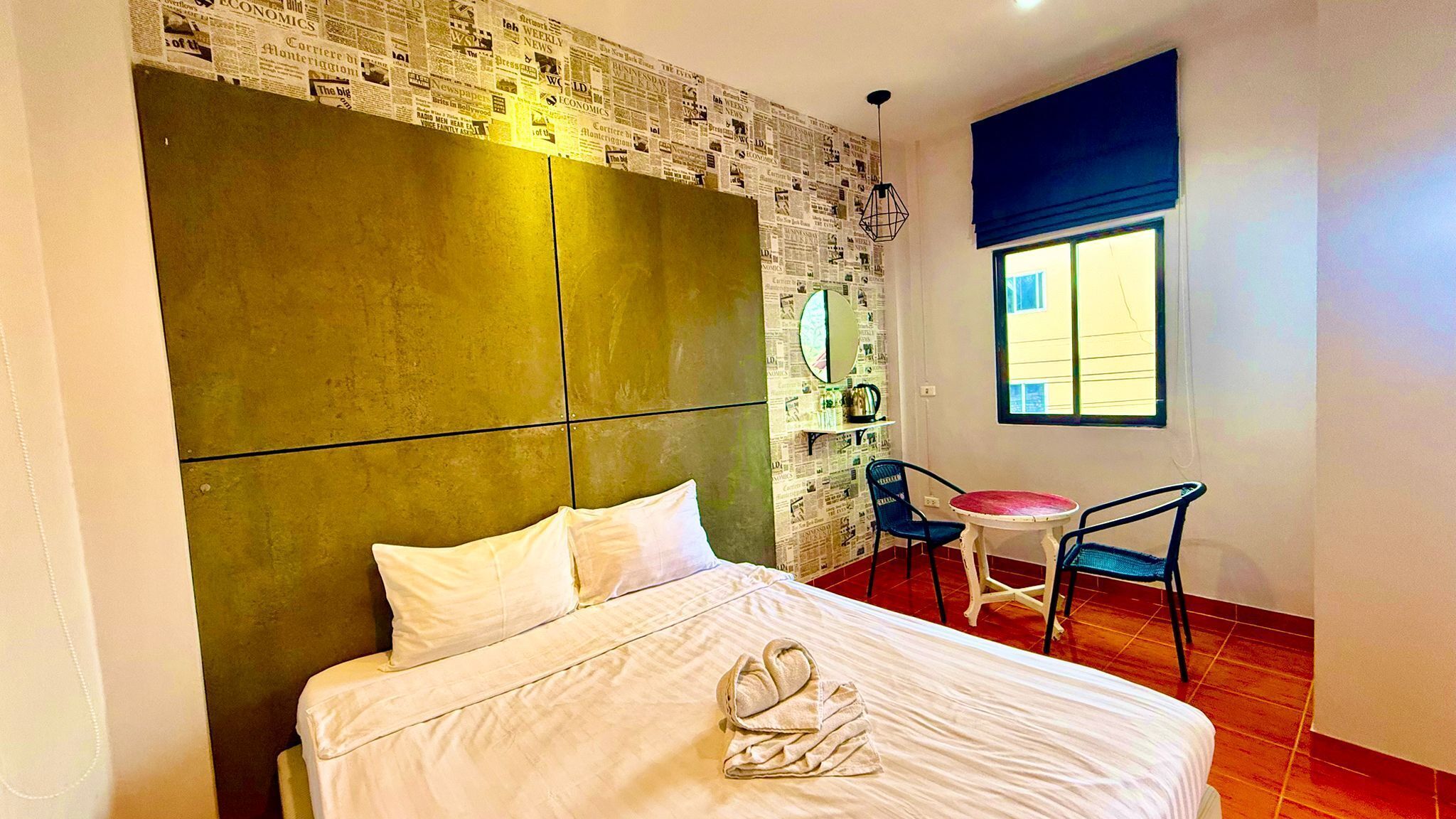 A hotel room with a large bed, a small table, two chairs, a mirror, and a window.