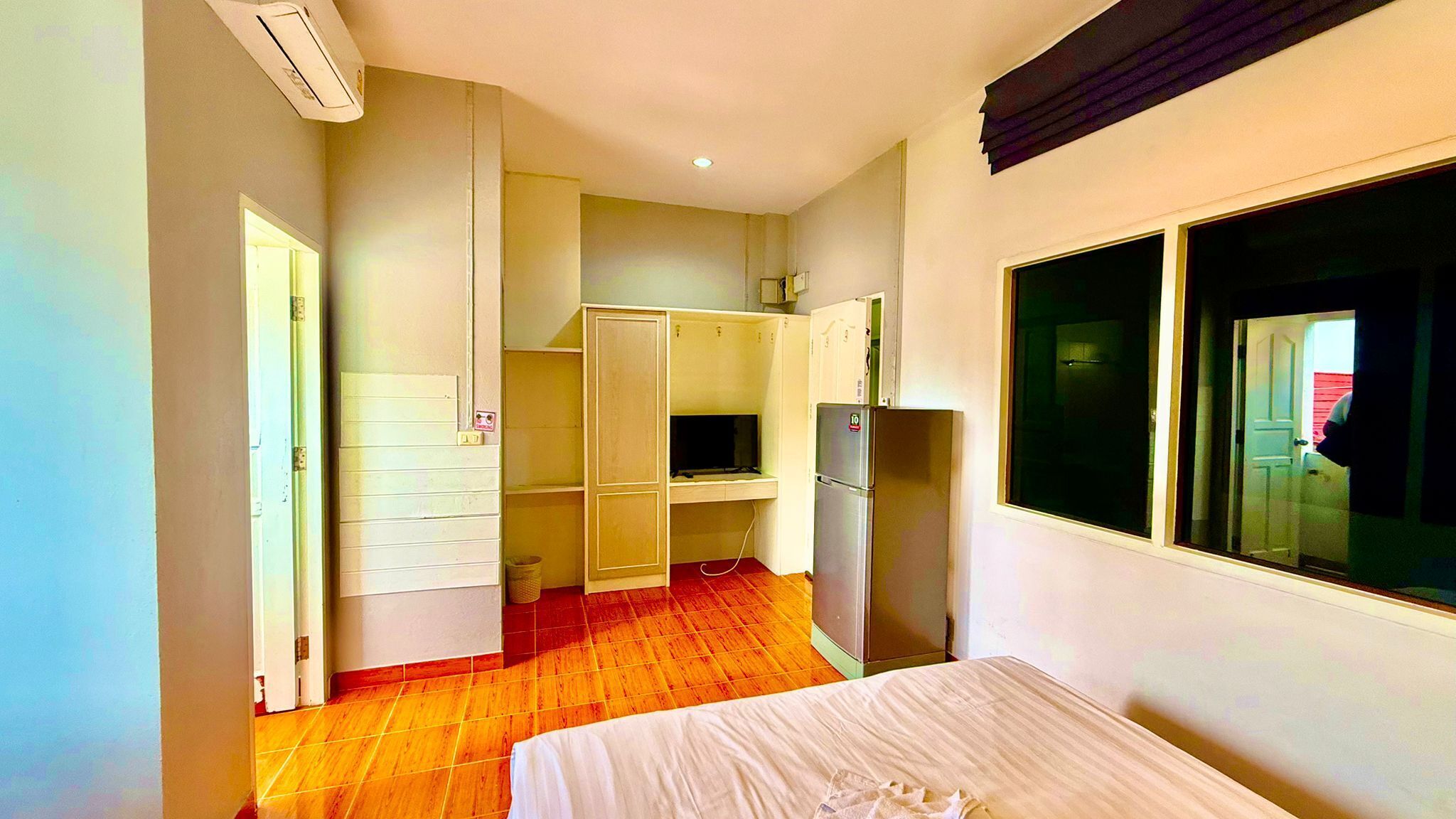 A compact hotel room with a bed, a kitchenette, a refrigerator, and a window.