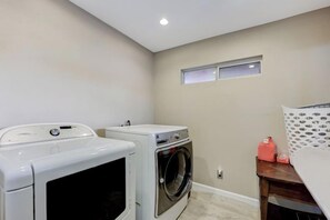 A laundry room with a washing machine, dryer, and a small table with a red container. - Strip-Side Villa, 6 Beds, Pool, Mini Golf, Karaoke (Las Vegas)