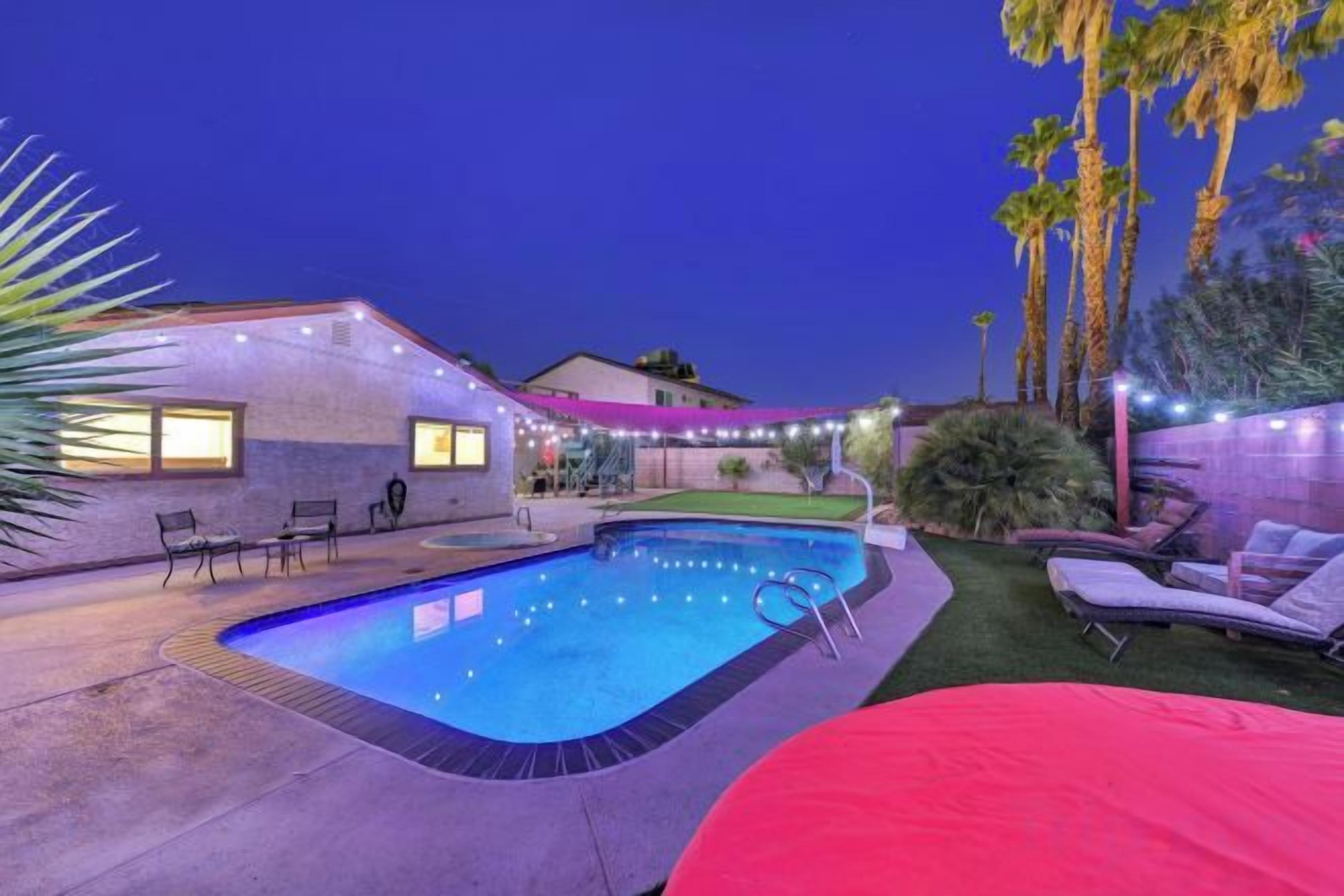 Una piscina con un deck alrededor, sillas de descanso y un patio cubierto.