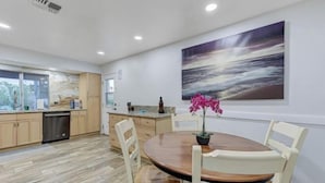 A modern kitchen with wooden cabinets, a dishwasher, and a dining area with a round table and chairs. - Strip-Side Villa, 6 Beds, Pool, Mini Golf, Karaoke (Las Vegas)