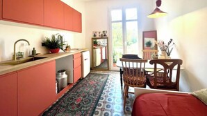 Una cucina compatta con un'ampia finestra, una zona pranzo con tavolo e sedie, e un letto rosso.