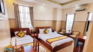Quarto de hotel com duas camas, uma escrivaninha de madeira, uma cadeira, uma mesa e um ventilador de teto.