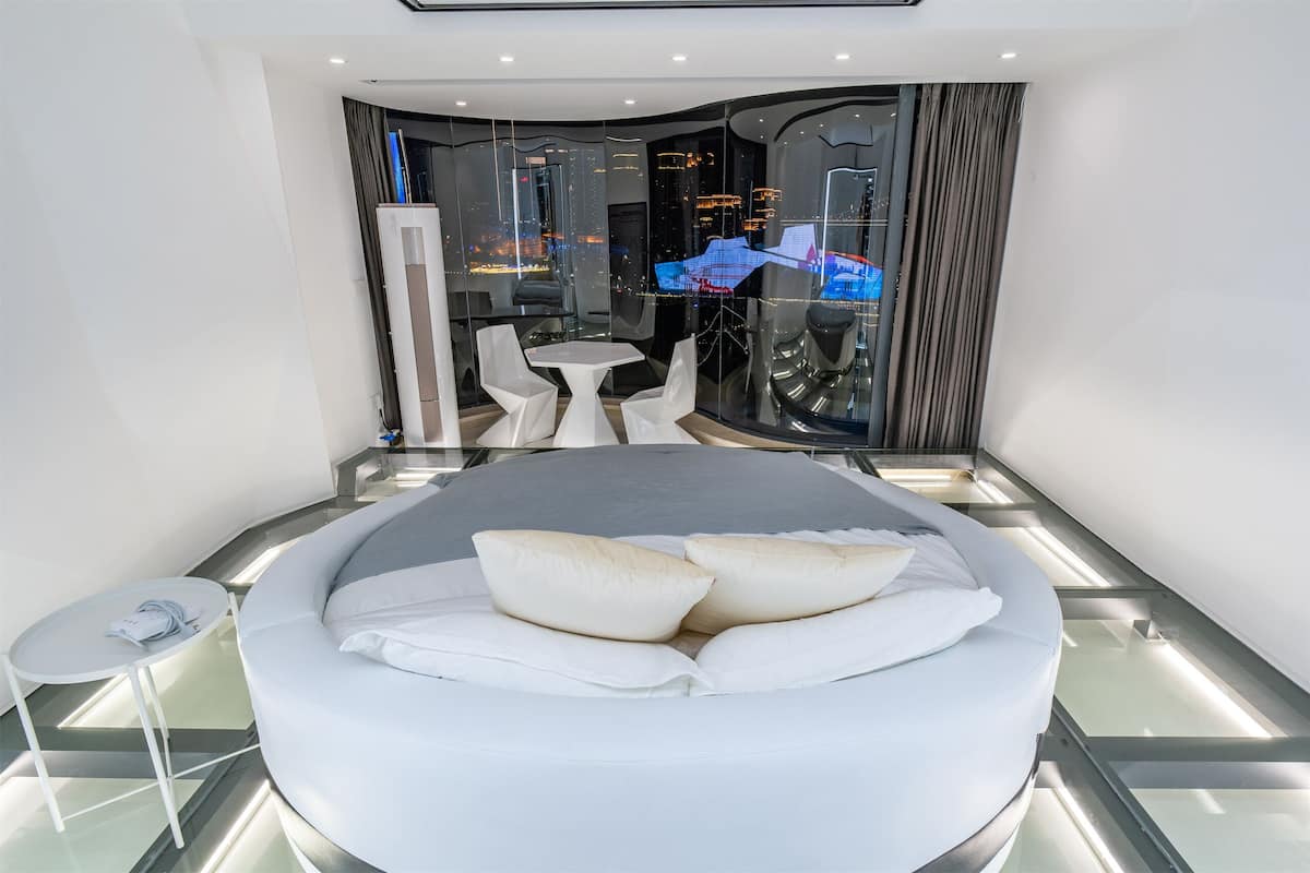 A modern hotel room with a large bed, a small table, and a seating area with chairs.