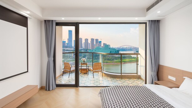 Une chambre d’hôtel avec un grand lit, un balcon offrant une vue sur les toits de la ville et un pont, ainsi qu’une petite table avec des chaises.