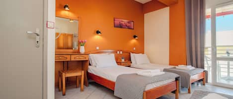 A hotel room with two beds, a desk, and a chair. There is a window with curtains, a painting on the wall, and a small table with a vase of flowers.