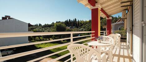 A balcony with white chairs and a table, overlooking a green landscape and buildings.