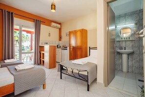 A hotel room with two beds, a kitchenette, a bathroom with a sink and mirror, and a balcony with curtains. - Solena Studios Kavos (Kavos)