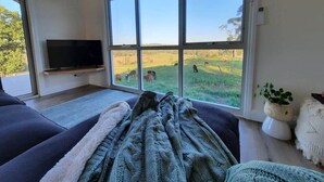 A modern living room with a large window, a flat-screen TV, and a cozy seating area. - Grasmere Lodge with Garden (Gruyere)