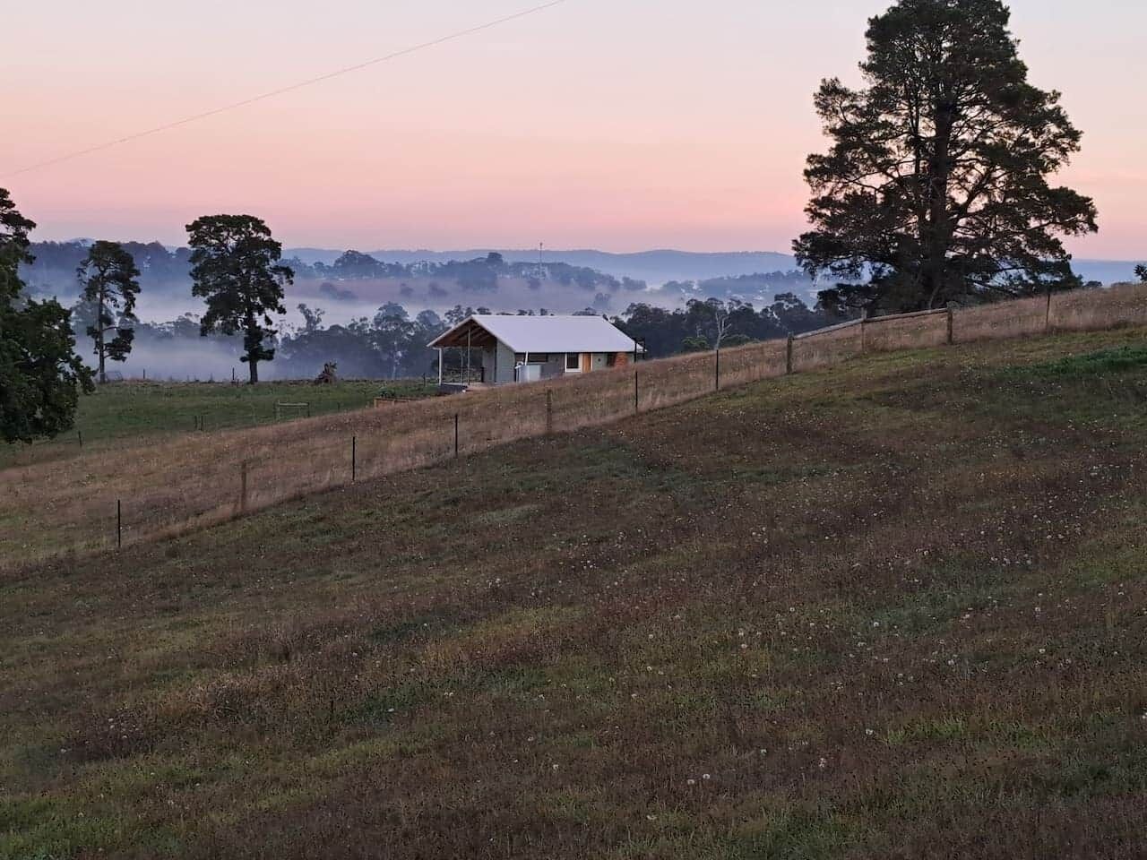 Een landelijk landschap met een klein huis op een heuvel, omringd door bomen en open velden.