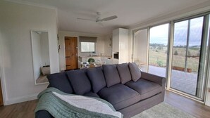 A modern living room with a dark grey sofa, a white ceiling fan, and a large sliding glass door leading to a patio. - Grasmere Lodge with Garden (Gruyere)