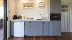 Une cuisine de taille réduite avec des meubles gris, un réfrigérateur blanc, une machine à café et une horloge au mur.