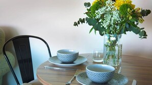 Une table de salle à manger ronde, sur laquelle sont posés deux bols décorés, un vase en verre avec des fleurs et un couteau.