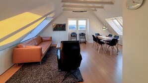 A loft-style apartment with a high ceiling, a dining area with a table and chairs, a sofa, and a large window. - Awesome home in Egernsund with house sea view (Egernsund)