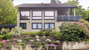 Ein zweistöckiges Haus mit Ziegelverkleidung, großen Fenstern und einem Garten mit verschiedenen Pflanzen und Blumen.