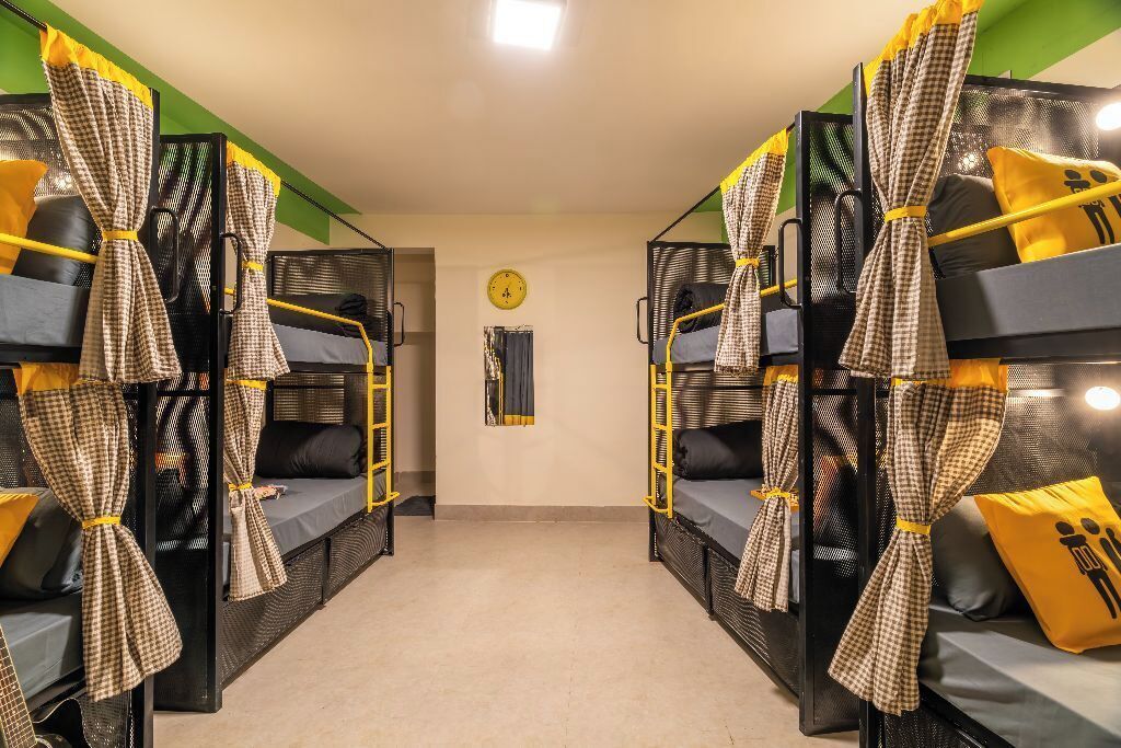 A dormitory room with bunk beds, checkered curtains, and a clock on the wall.