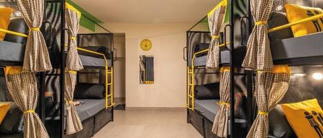 A dormitory room with bunk beds, checkered curtains, and a clock on the wall.