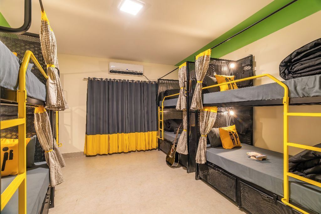 A dormitory room with bunk beds, a curtain, an air conditioning unit, and a small table.