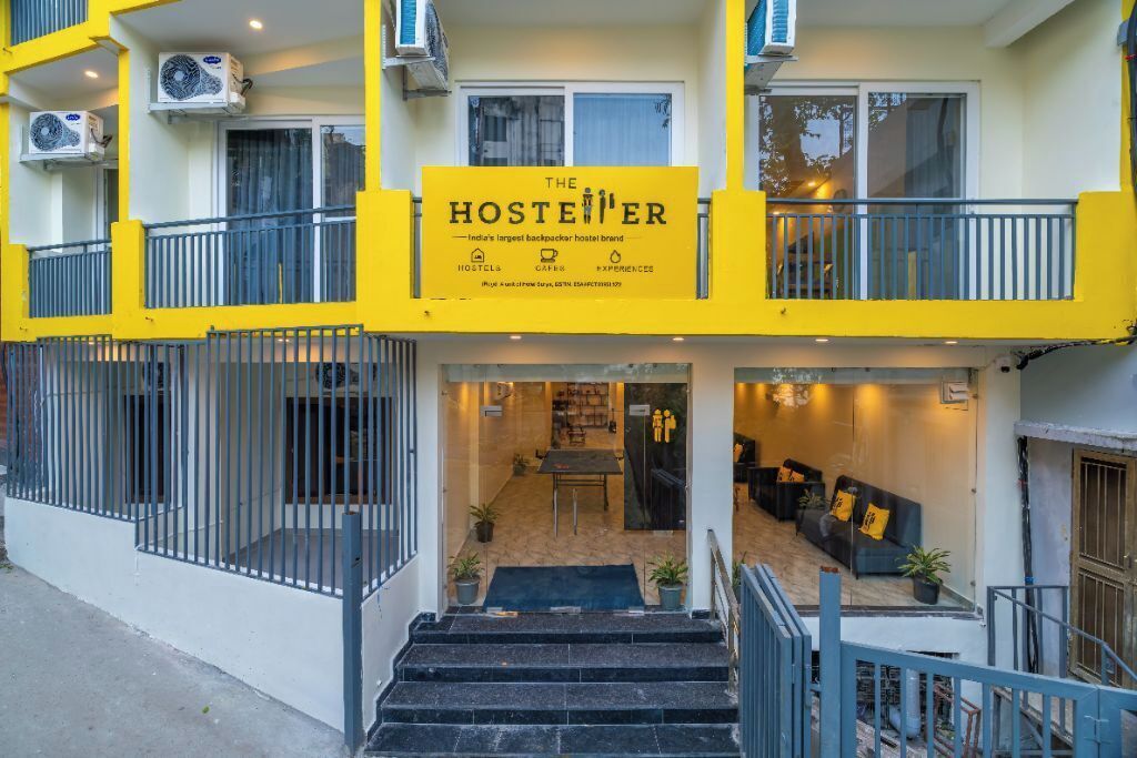 A hostel with a bright yellow facade, a staircase leading to the entrance, and a seating area with cushions.
