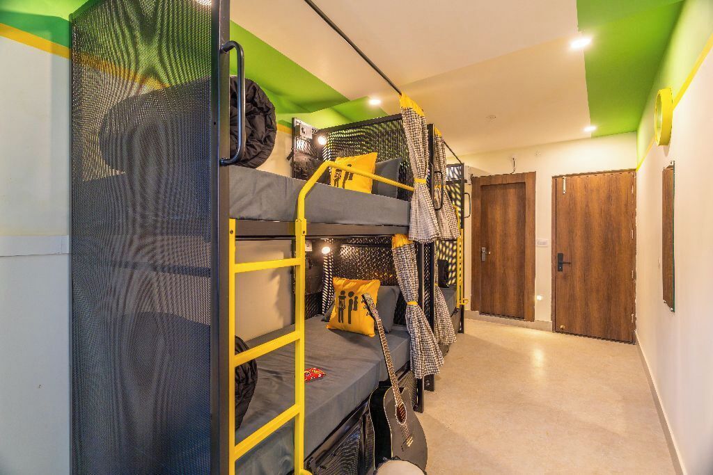 Une chambre de dortoir avec des lits superposés, une porte moustiquaire et, au fond, une porte en bois.