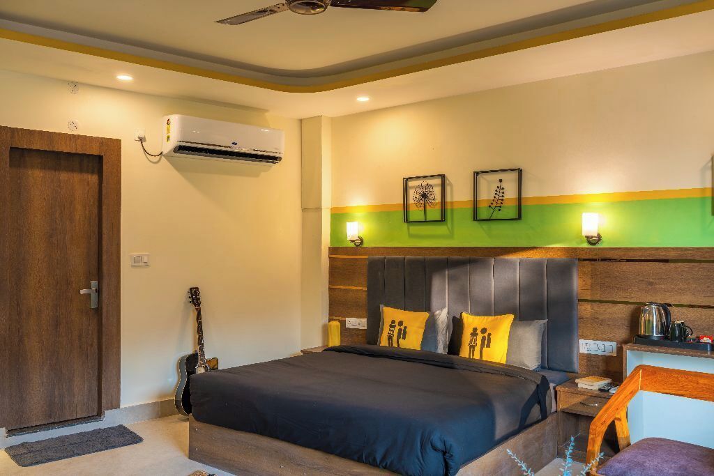 A bedroom with a bed, a guitar, a wooden door, and an air conditioning unit.
