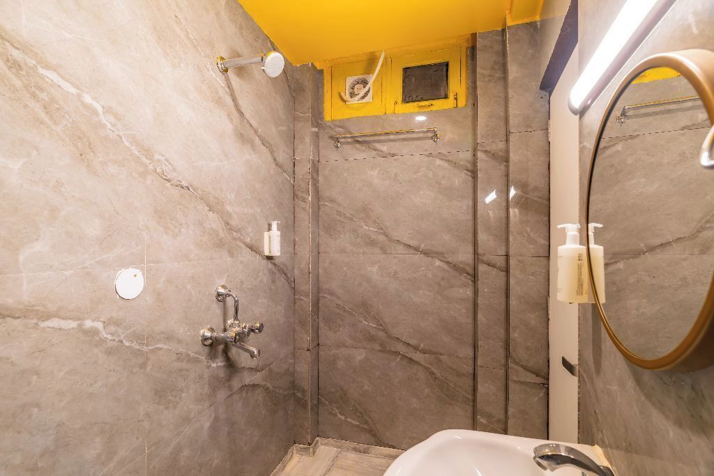 A bathroom with a marble wall, a yellow ceiling, a shower area, and a sink with a mirror.