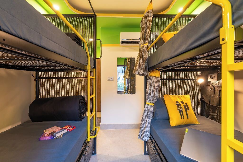 Camera con letto a castello, parete verde, una piccola finestra e cuscino giallo.
