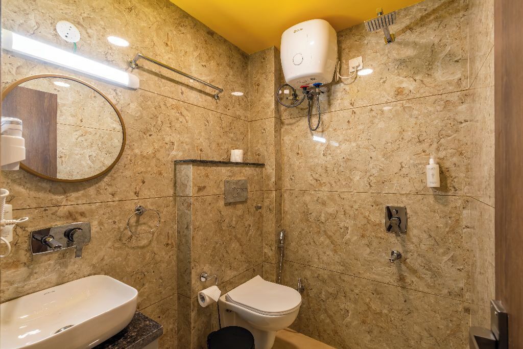 A bathroom with a marble wall, a sink, a toilet, a shower, and a mirror.