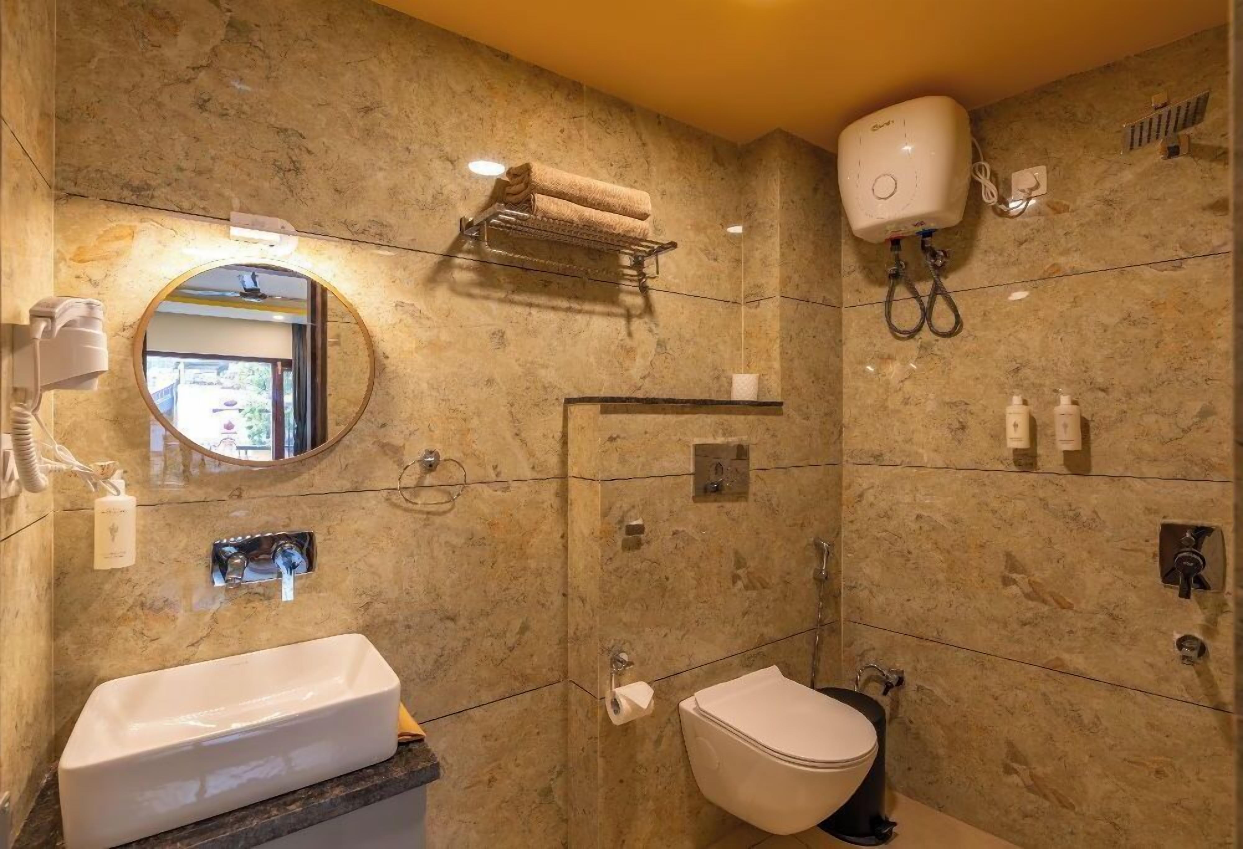 A bathroom with a marble wall, a sink, a toilet, a towel rack, and a handheld showerhead.