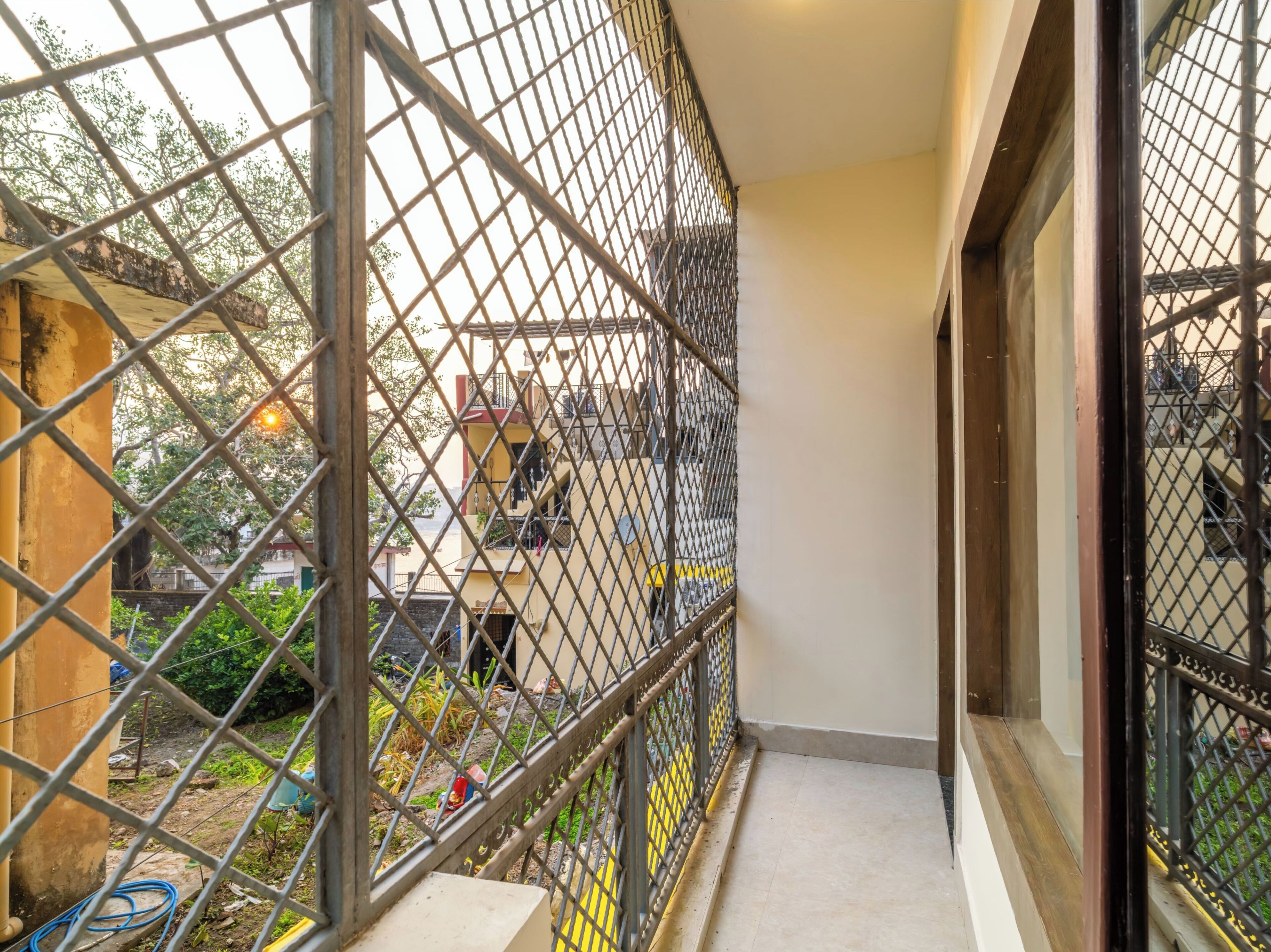 Un balcon étroit avec des balustrades en métal, un sol carrelé et une vue sur des bâtiments et de la verdure en arrière-plan.