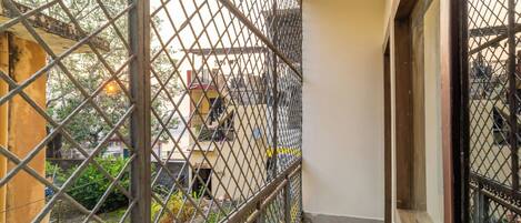 Un balcon étroit avec des balustrades en métal, un sol carrelé et une vue sur des bâtiments et de la verdure en arrière-plan.