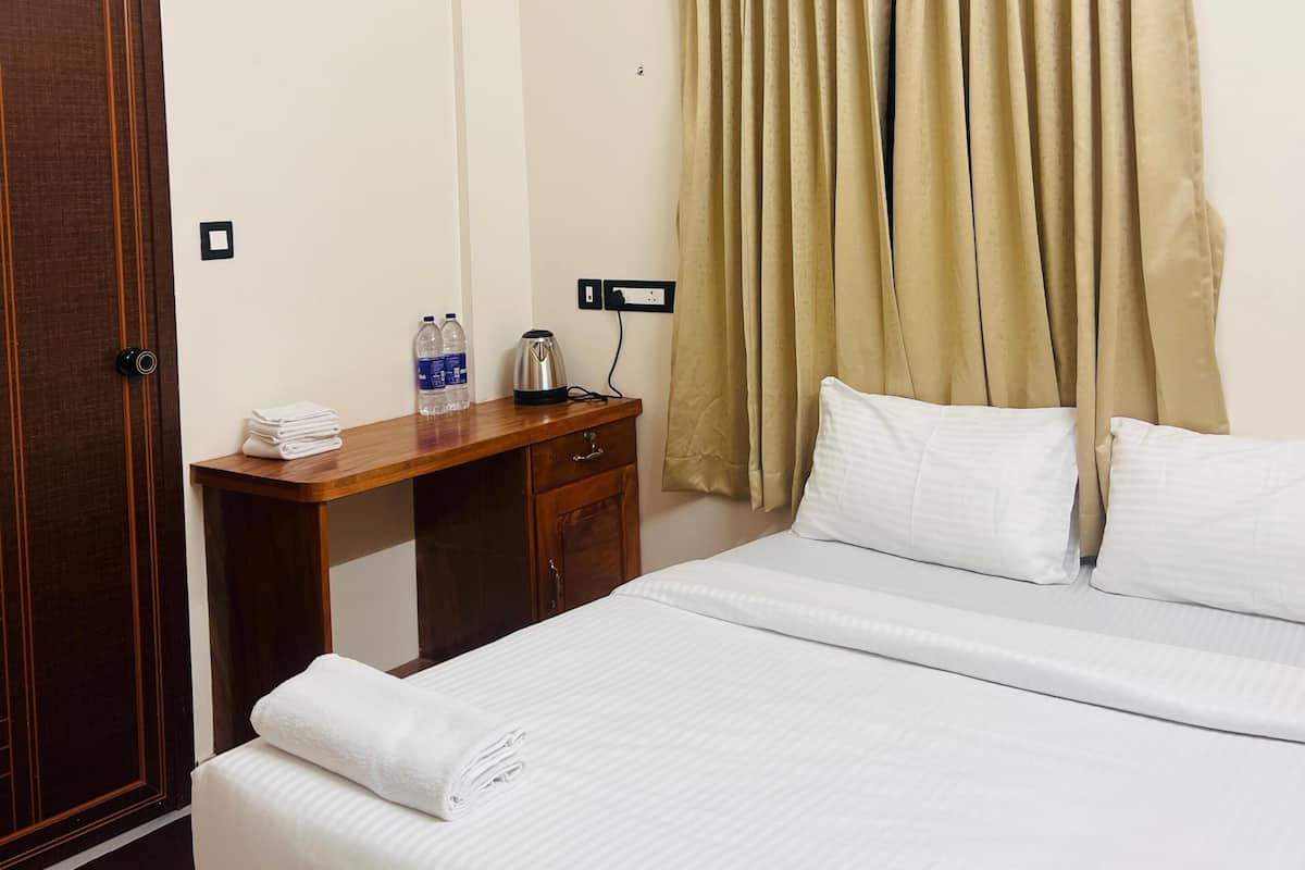 A hotel room with a bed, a desk, a wardrobe, an air conditioning unit, and a ceiling fan.