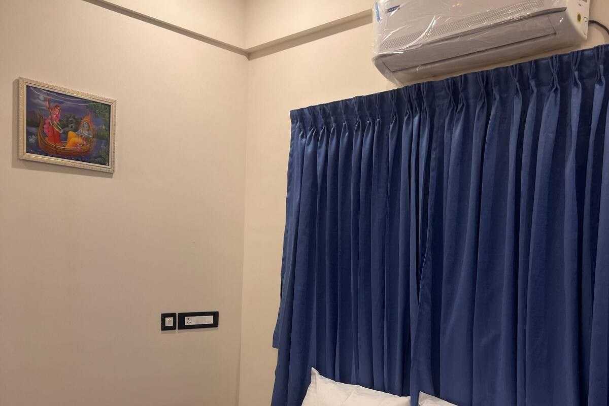 A hotel room with a bed, a painting on the wall, and an air conditioning unit.