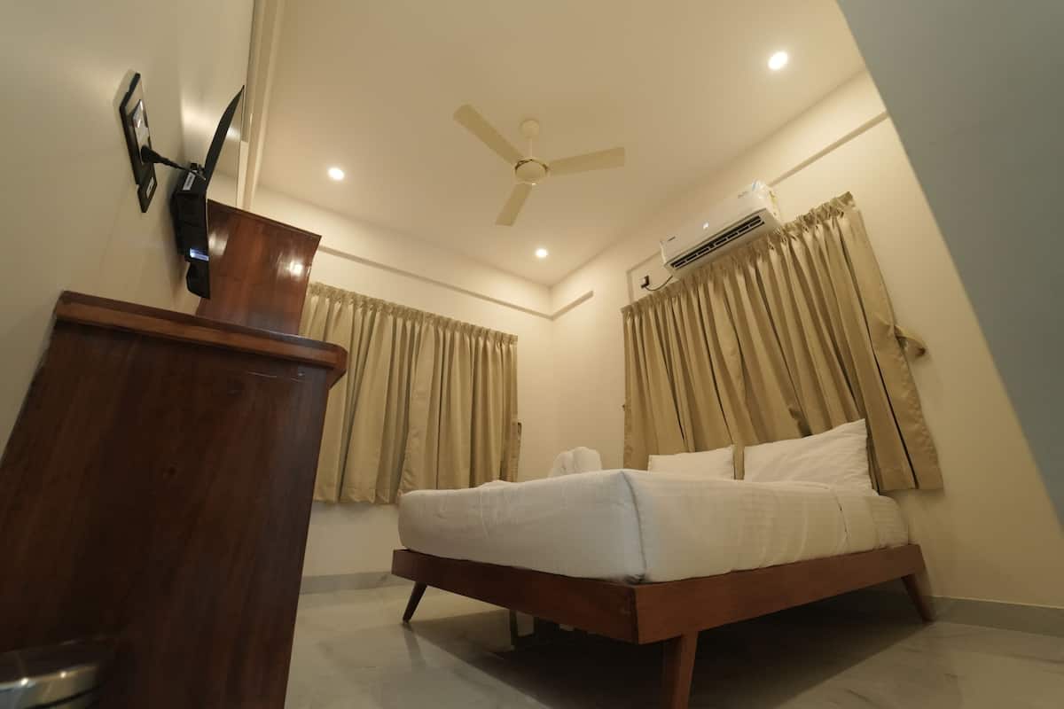 A bedroom with a bed, wooden dresser, ceiling fan, air conditioning unit, and curtains.
