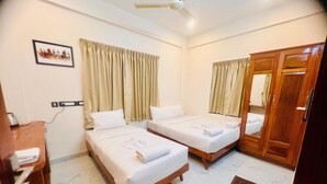 A hotel room with two beds, a wooden wardrobe, a ceiling fan, and a wall-mounted power outlet. - Vallimony Luxury Stays-Padmanabha Temple (Thiruvananthapuram)