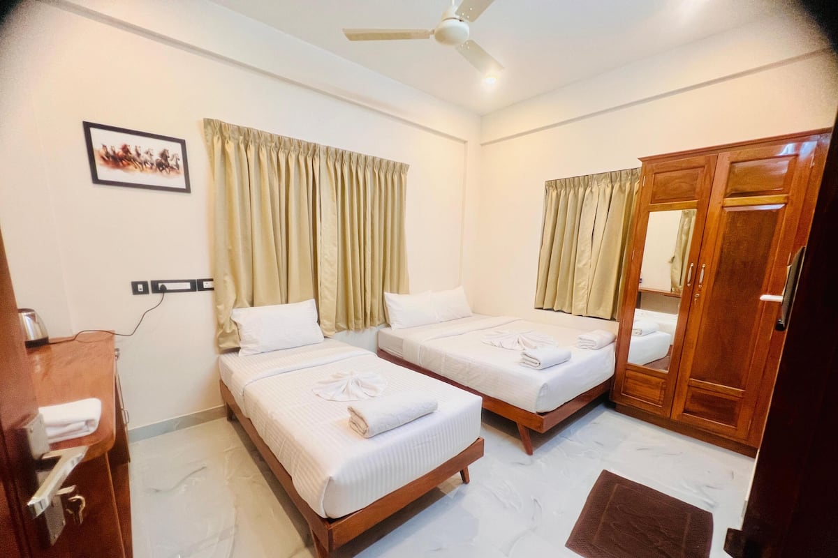 A hotel room with two beds, a wooden wardrobe, a ceiling fan, and a wall-mounted power outlet.