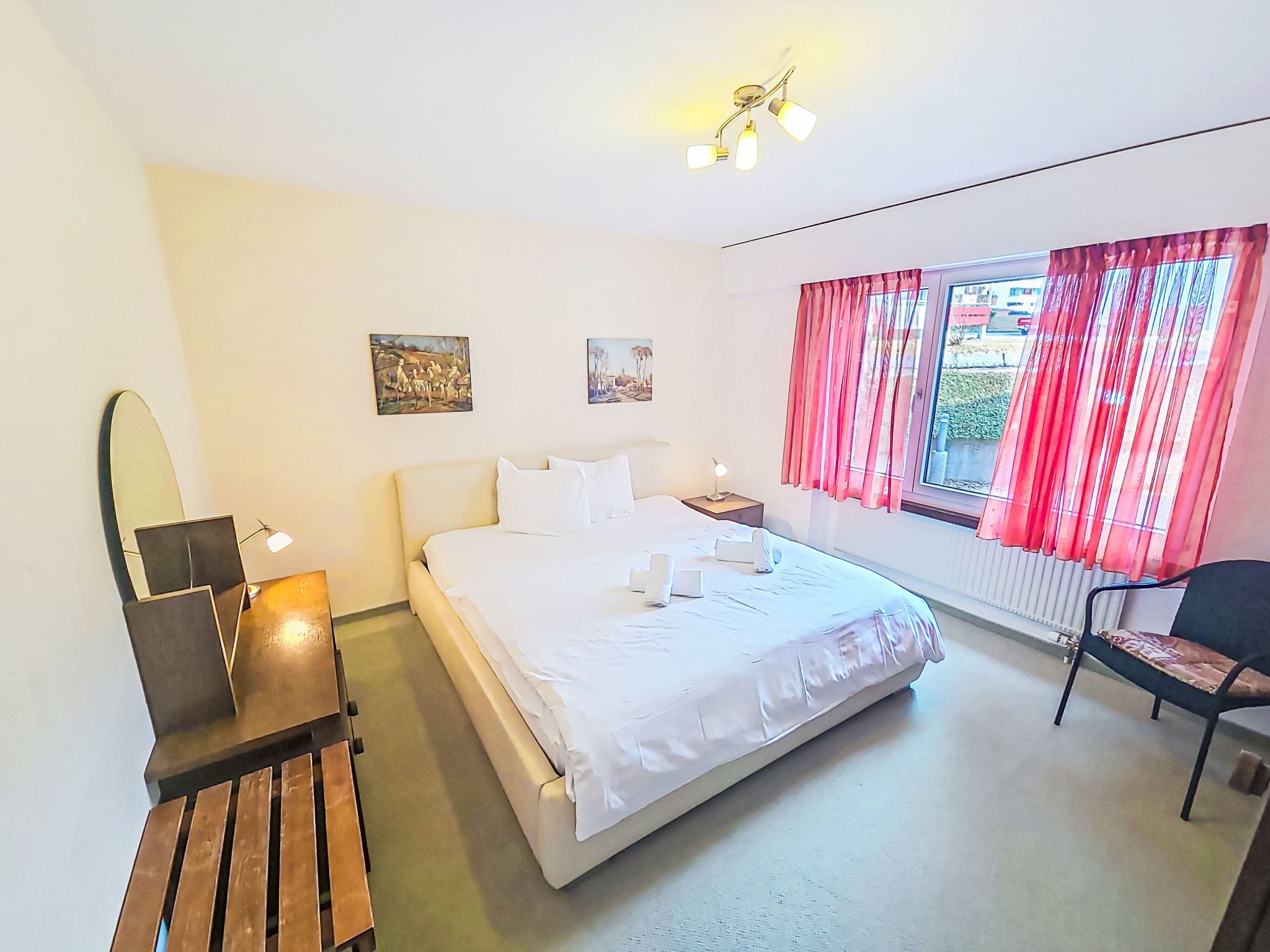 A bedroom with a bed, bedside tables, a chair, a desk, and a window with curtains.
