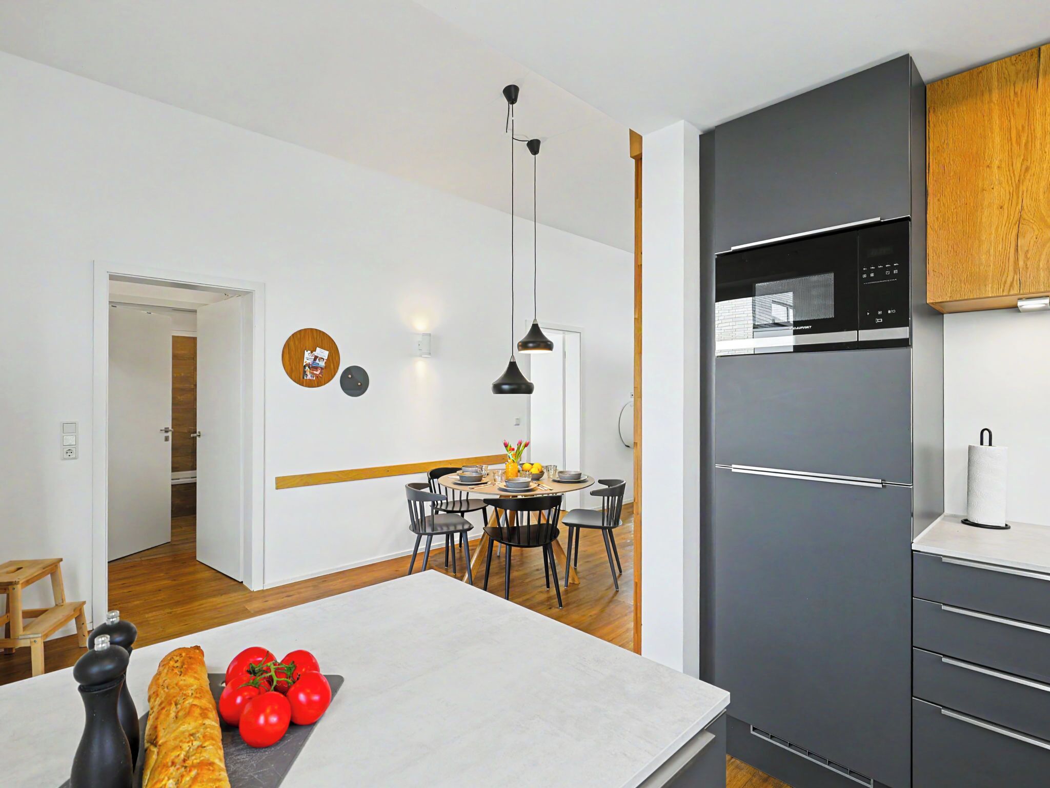 Una cocina moderna con refrigerador empotrado, armarios de madera y un comedor con mesa y sillas.