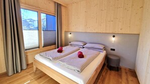 Een slaapkamer met houten lambrisering, een groot bed, twee nachtkastjes, een kleine prullenbak en een raam met gordijnen.