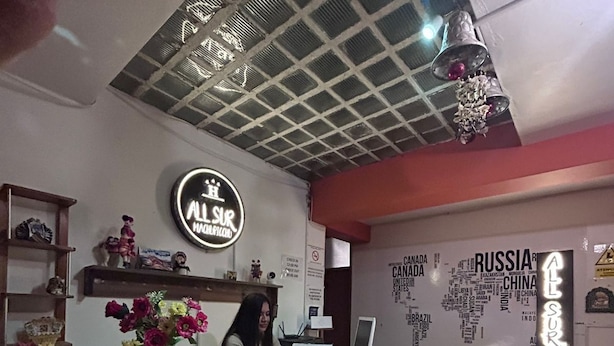 A reception desk with a marble top, a woman seated behind it, and a wall with country names. - All sur machupicchu  (Aguas Calientes)