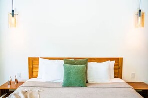 A neatly made bed with a wooden headboard, two bedside tables, and a green pillow. - New authentic Jungle Gem (Nosara)