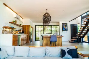 A modern kitchen with wooden cabinets, a stainless steel refrigerator, and a dining area with a chair and table. - New authentic Jungle Gem (Nosara)