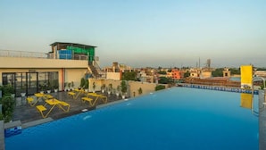 Una piscina sul tetto con sedie a sdraio gialle, una piattaforma da tuffo e vista sulla città.