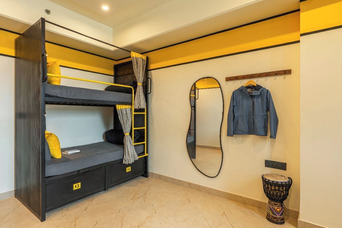 A bunk bed with a ladder, a mirror, a hanging jacket, and a drum.