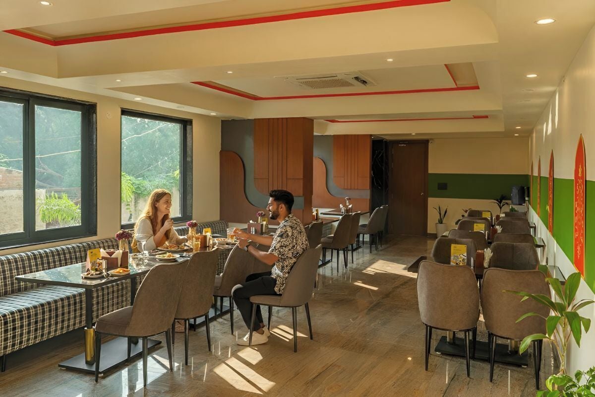 En modern restaurang med en blandning av olika sittalternativ, inklusive bord och bänkar, stora fönster som släpper in naturligt ljus och en stilren, modern inredning.