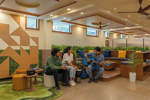 A modern lounge area with a geometric wall design, comfortable seating, and a guitar player. - The Hosteller Agra Tajganj (Agra)