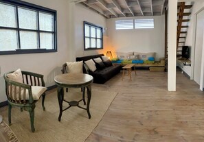 A spacious living area with a sofa, a wooden chair, a small table, and a lamp. There are windows providing natural light and a staircase leading to another level. - Moorea Fare Korail-private pool and sea access-Temae (Moorea)