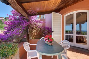 A patio with a table and chairs, a door with glass panels, and purple flowering plants. - Villa Fiorita - Bouganville Apartment: Sea View, Private Pergola, Near Morcone Beach (Capoliveri)